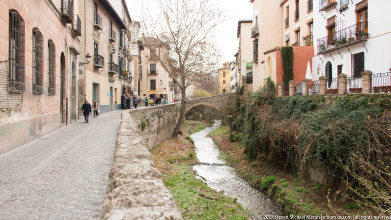 Cobbled Carrera del Darro beside the narrow Darro River, lined with historic houses and balconies in Granada.