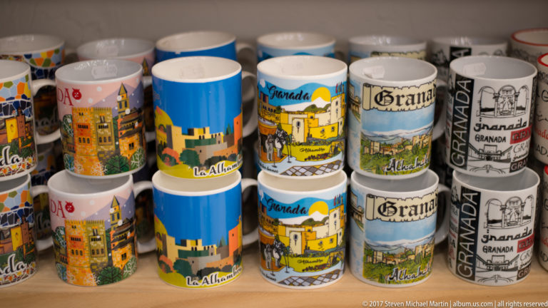 Rows of colorful ceramic souvenir mugs printed with Granada, Alhambra, and Albaicín designs.