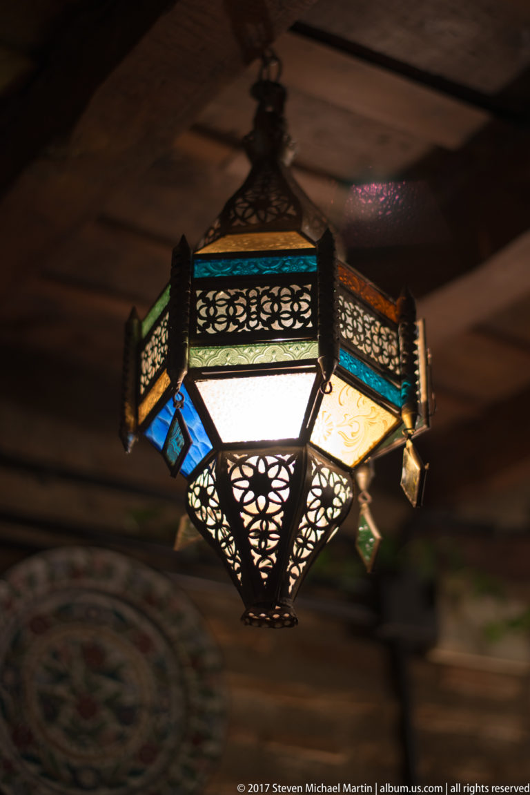 Geometric hanging lantern with pierced dark metal and blue, amber, and pale glass panels.