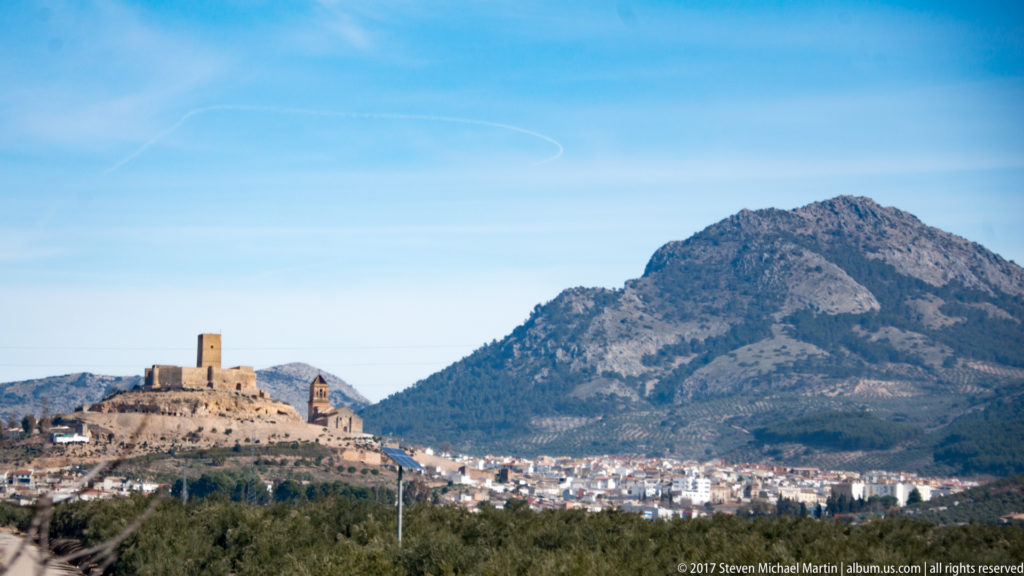 White town below a small fortified hill and large rocky mountain in the Granada region.