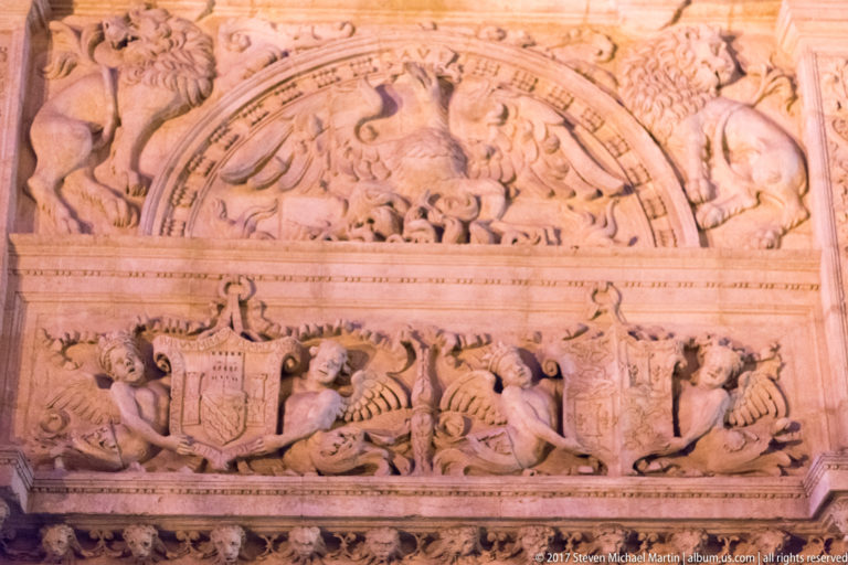 Close view of a Renaissance stone relief with heraldic shield, scrollwork, figures, creatures, and carved heads.
