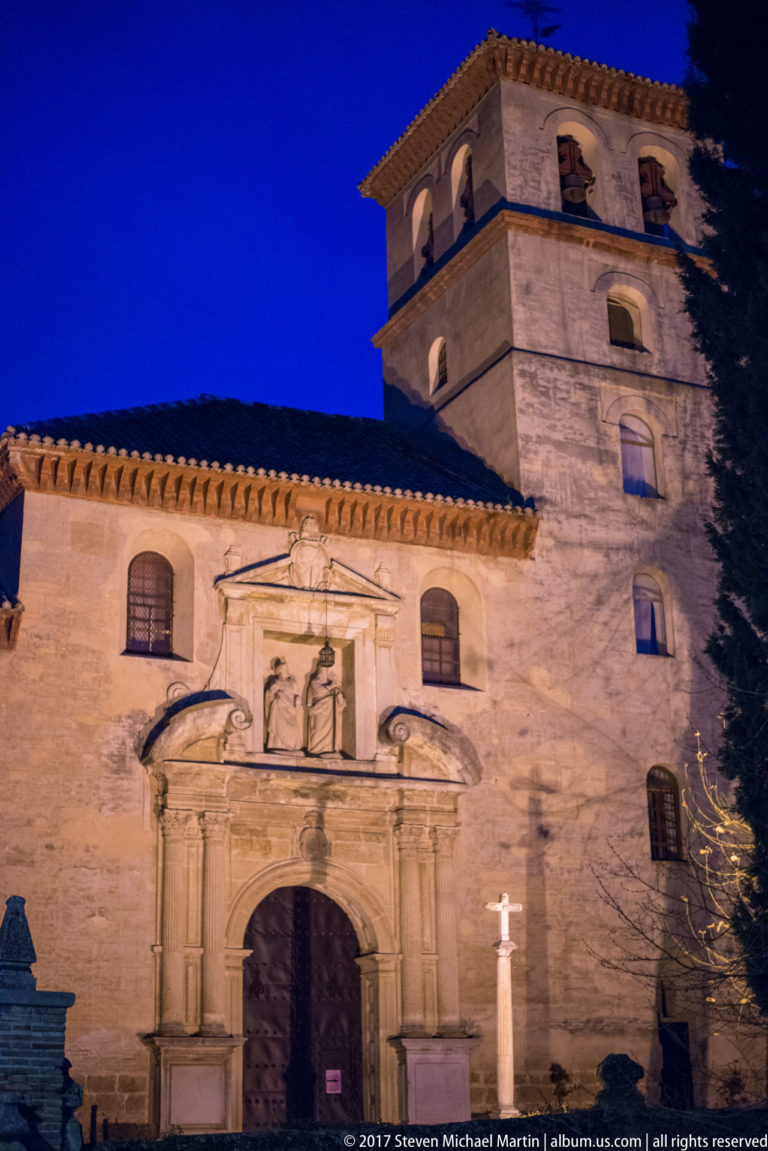 Floodlit San Gil y Santa Ana church with sculpted portal and square bell tower against a deep blue sky.