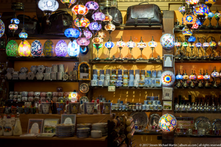 Shelves packed with colorful mosaic lamps, painted mugs, plates, glassware, and leather souvenirs.