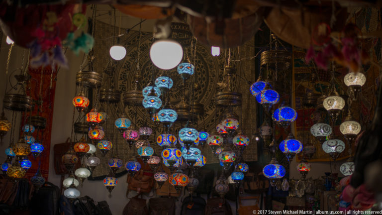 Clusters of glowing blue, red, orange, and white patterned hanging lamps in a Granada shop.