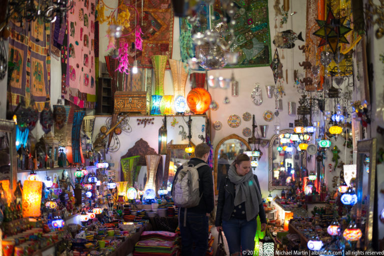 Two visitors inside a crowded Granada shop filled with colorful lamps, textiles, ceramics, and souvenirs.
