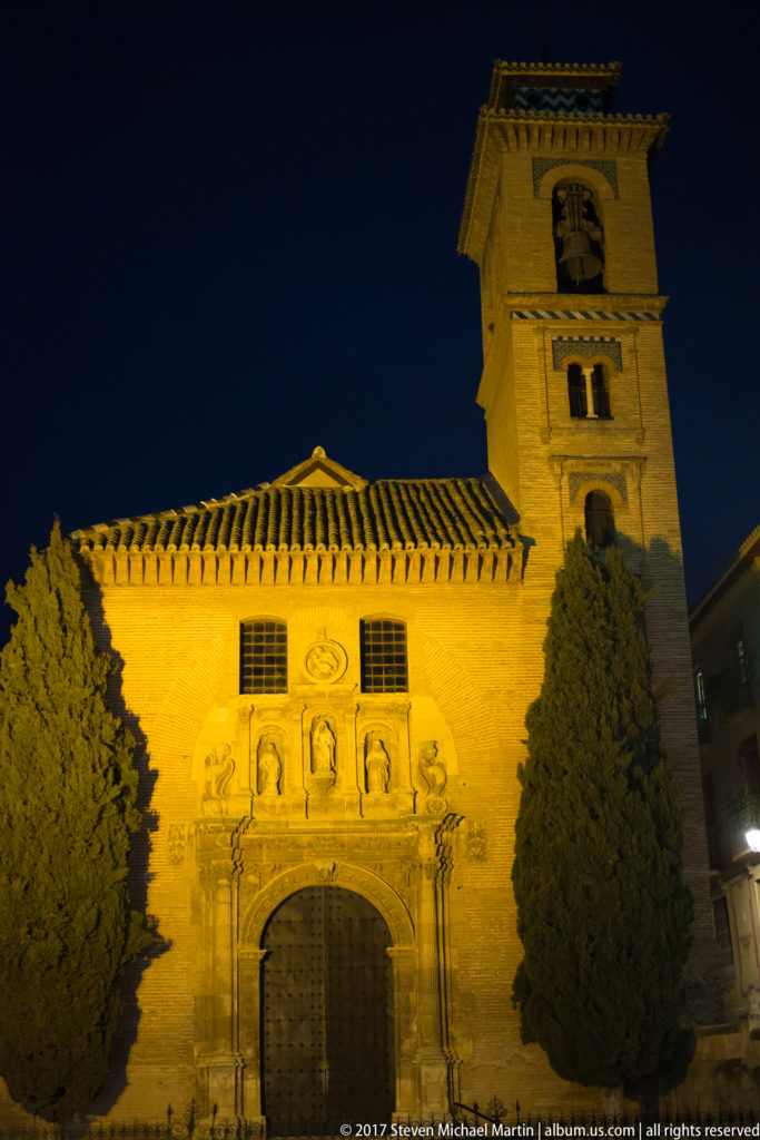 Illuminated Church of San Gil y Santa Ana with Renaissance portal and square bell tower at night.