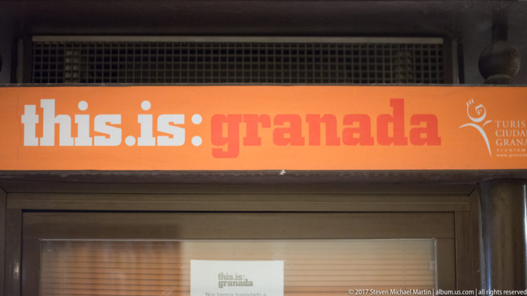 Orange “this.is:granada” sign above a storefront doorway in Granada.