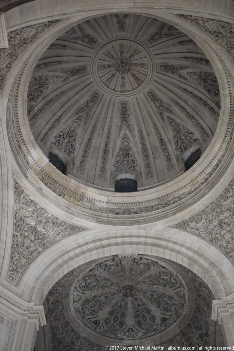 Oblique upward view of two decorated circular vaults separated by a broad arch in Granada Cathedral.