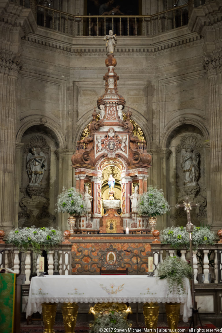 Polychrome red-and-gold altar structure with flowers and sculpted figures inside Granada Cathedral.
