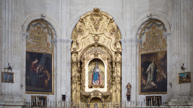 Gilded Baroque side-chapel altarpiece between two large paintings inside Granada Cathedral.