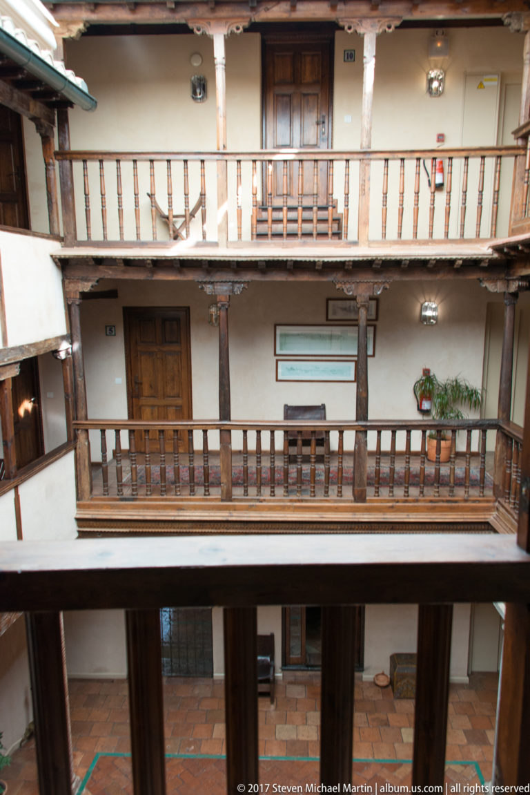 Three-story interior courtyard with wooden galleries, balustrades, tiled floors, and guest-room doors in Granada.
