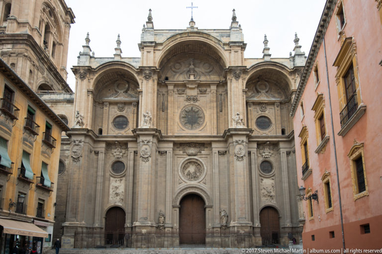 Main façade of Granada Cathedral with three arched bays, classical columns, round windows, and tall portals.
