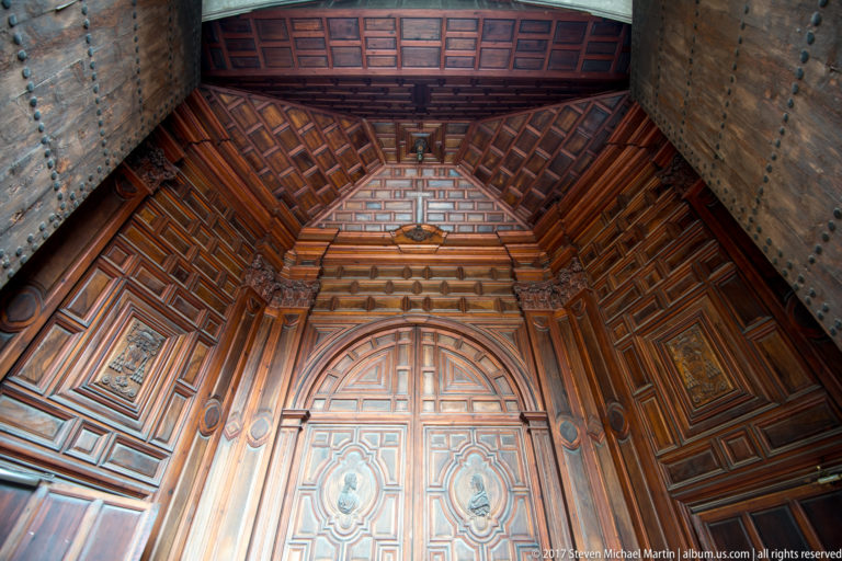 Elaborately paneled wooden entrance enclosure with coffered canopy and studded outer doors inside Granada Cathedral.