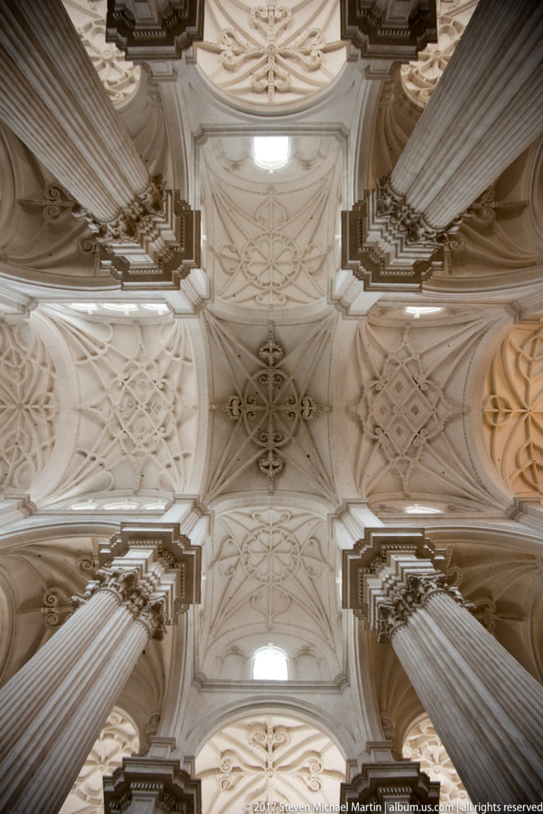 Long upward view of patterned cathedral vaults receding between massive fluted piers and bright clerestory openings.