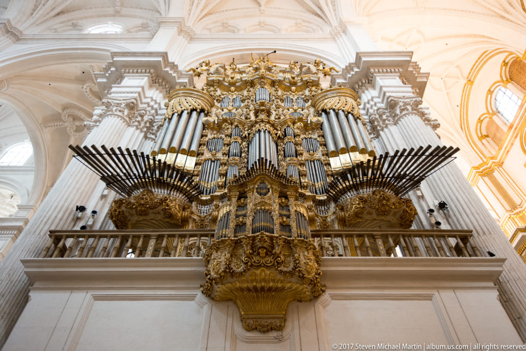 Large gilded pipe organ with vertical pipes and projecting trumpet ranks above a gallery in Granada Cathedral.