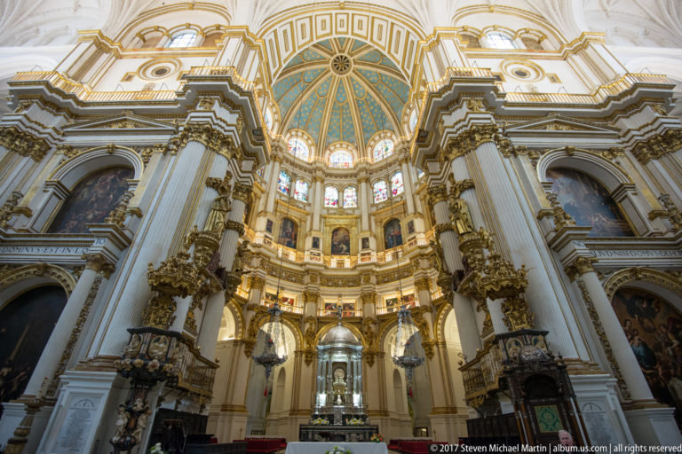 Granada Cathedral Capilla Mayor with towering white columns, gilded decoration, paintings, and a blue-and-gold dome.