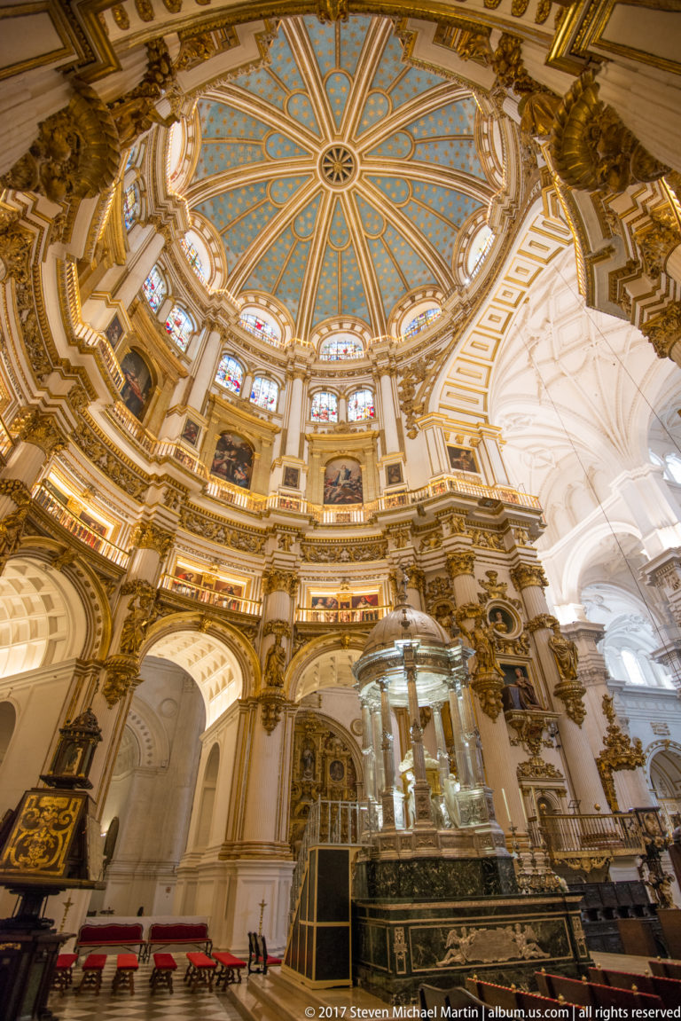 Oblique interior of Granada Cathedral's Capilla Mayor beneath a blue-and-gold dome with stained-glass windows.