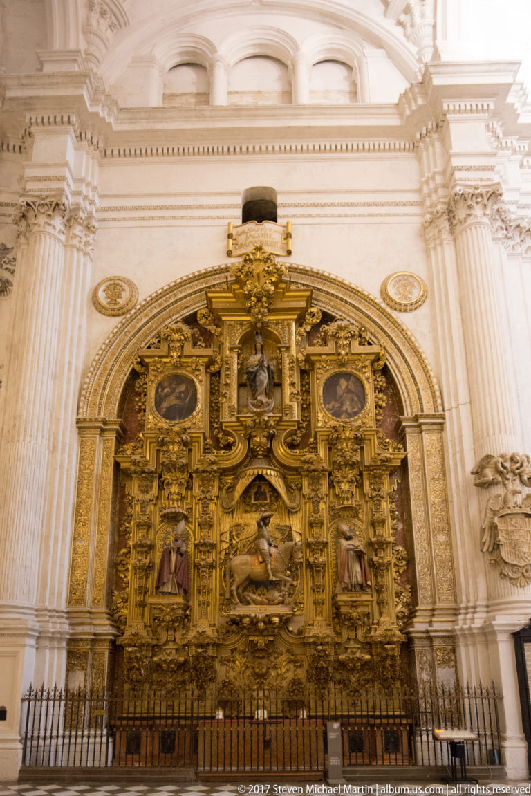 Ornate gilded side-chapel retable with central sculpture and medallions beneath a pale stone arch in Granada Cathedral.