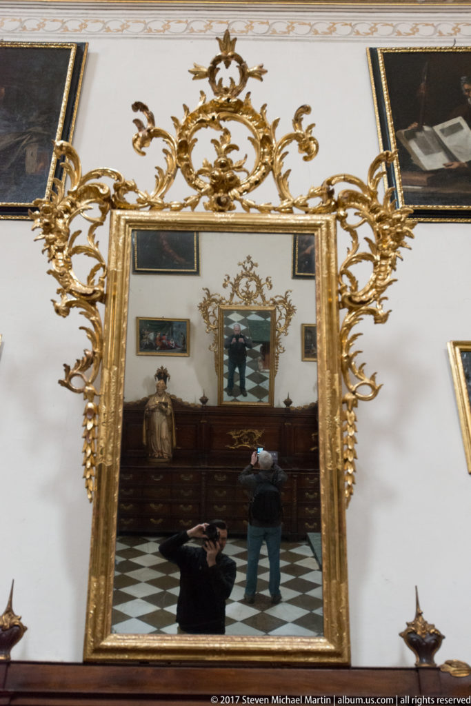 Large ornate gilded mirror with scrolling foliage above dark wooden cabinetry in Granada Cathedral's sacristy.