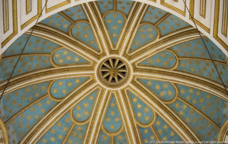 Blue radial dome covered with gold stars and divided by pale gilded ribs in Granada Cathedral.