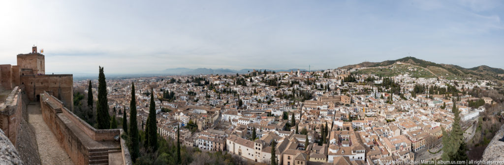 Alhambra wall and cypress trees in the foreground with the densely built Albaicín hillside rising beyond.
