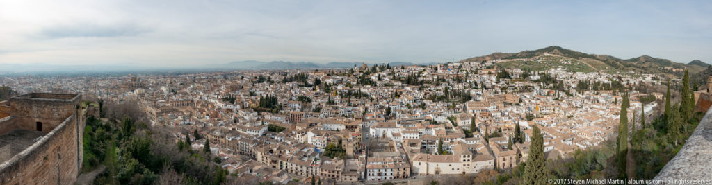 Panoramic view of densely packed white houses and terracotta roofs climbing the Albaicín hillside opposite the Alhambra.