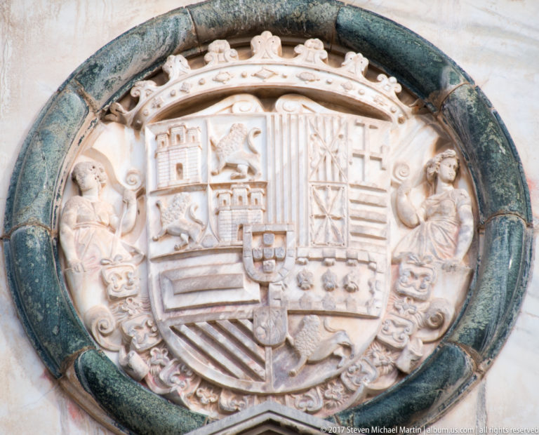 Circular carved coat of arms of Emperor Charles V with an imperial crown, quartered shield, and flanking Pillars of Hercules.