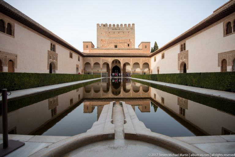 Centered view across the Court of the Myrtles reflecting pool toward the arcaded façade and square Comares Tower.