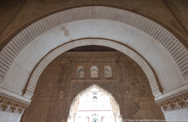 Large pale horseshoe arch framing a smaller decorated opening and bright palace façade beyond.