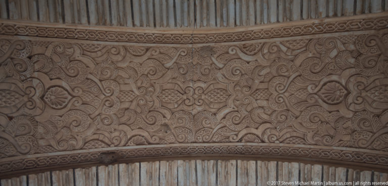 Close view of pale carved stucco with scrolling vegetal motifs, palmettes, and narrow geometric borders.