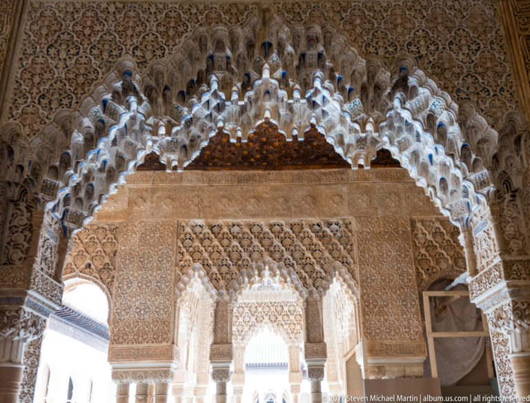Large muqarnas-edged Nasrid arch with dense carved stucco framing a second decorated opening beyond.