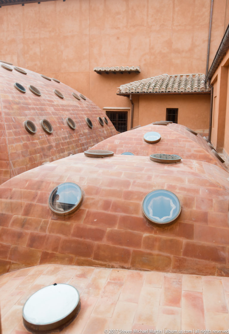 Terracotta-clad domed roofs with several round glazed skylights set between ochre palace walls.
