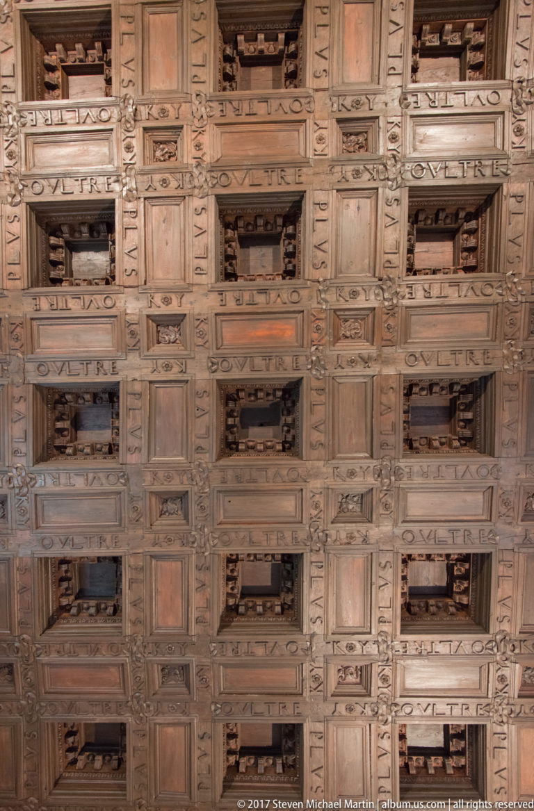 Rectangular wooden coffered ceiling with carved moldings, recessed panels, and repeated inscriptions.