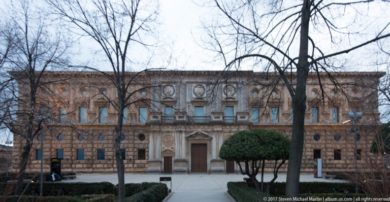 Front façade of the Palace of Charles V with rusticated stonework, rectangular windows, circular openings, and a central classical doorway.