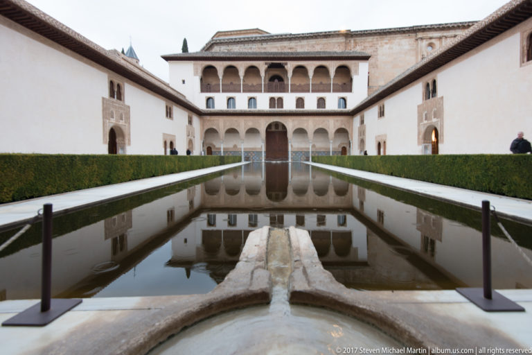 Long reflecting pool bordered by clipped hedges, aligned with the arcaded Comares façade at the far end of the Court of the Myrtles.