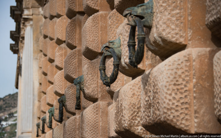 Oblique close view of rusticated stone blocks with a row of green-patinated bronze ring handles on the Palace of Charles V.
