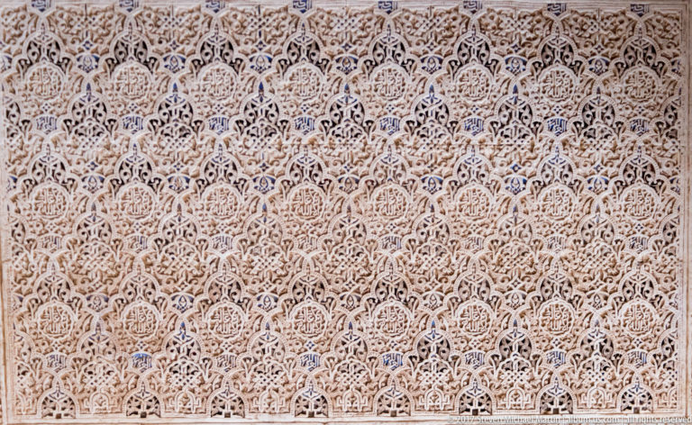 Large wall panel covered with finely carved pale stucco arabesques and repeated geometric motifs.