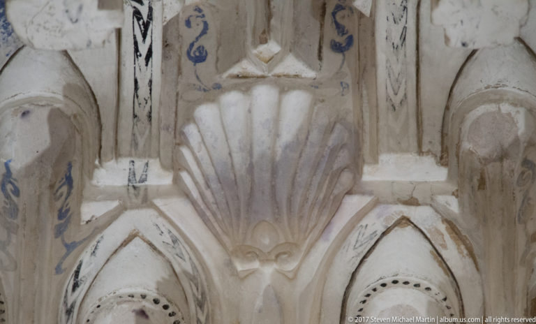 Close view of white Nasrid muqarnas plasterwork with layered niches, shell motifs, and traces of blue pigment.