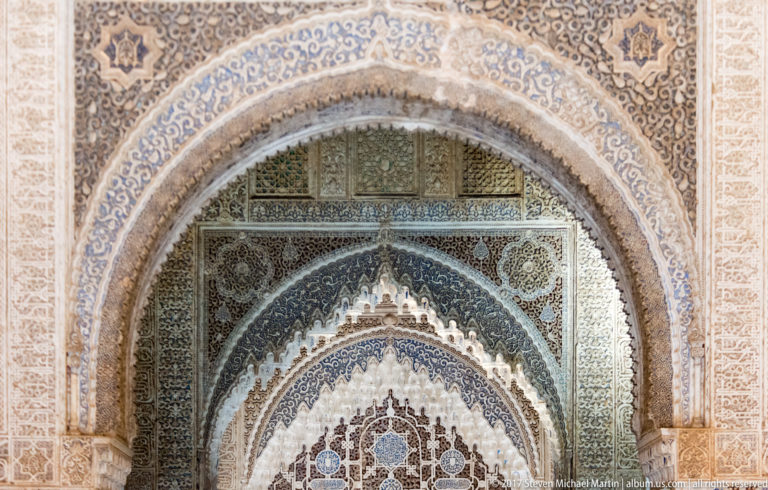 Nasrid horseshoe arch covered with carved Arabic inscriptions, geometric ornament, arabesques, and surviving blue polychromy.
