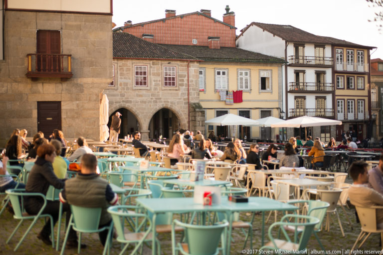 Busy outdoor café seating fills a historic Guimarães square lined with arcaded stone buildings and traditional façades.