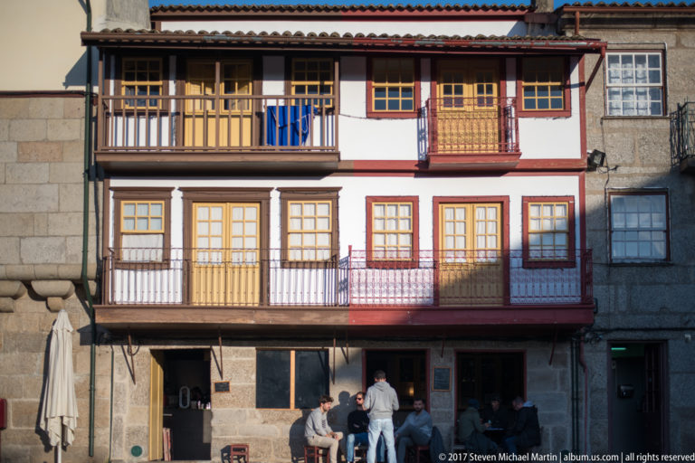 Three-story traditional house with stacked timber balconies, colorful window frames, glazed doors, and granite ground floor.