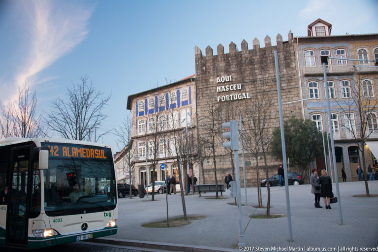 Crenellated stone Torre da Alfândega with large “AQUI NASCEU PORTUGAL” inscription beside a city bus and historic façades.