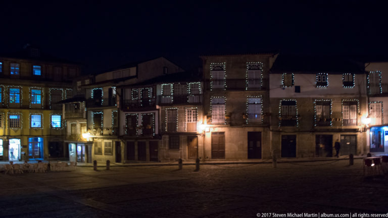 Historic Guimarães square at night with window outlines traced in decorative lights and warm streetlamps illuminating stone paving.