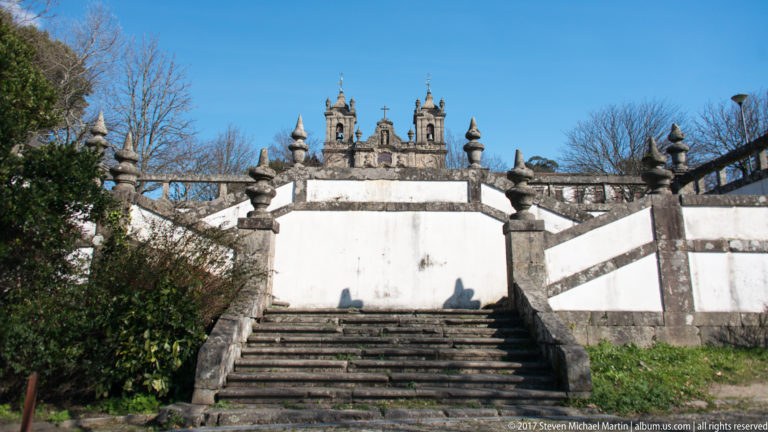 Weathered stone steps rise to a white terrace with decorative finials, while church towers and pinnacles appear above the wall.