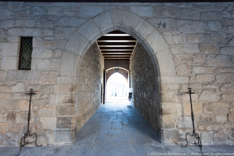 Pointed granite arch leading through a narrow passage, flanked by wrought-iron torch stands in massive stone walls.