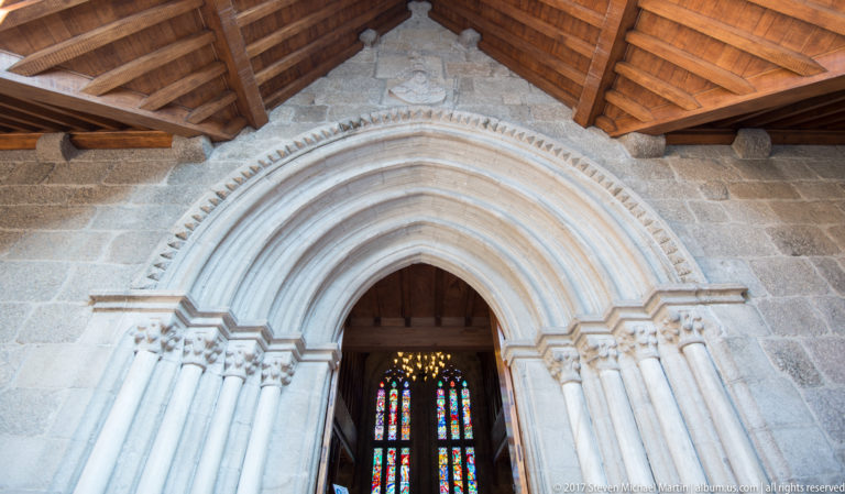 Pointed stone chapel portal with multiple archivolts, slender colonnettes, carved capitals, and stained glass visible through the doorway.