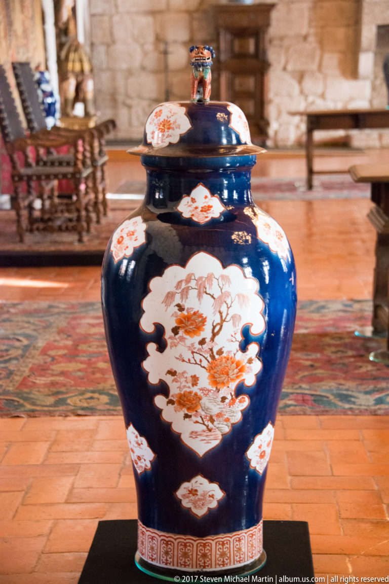Large cobalt-blue lidded porcelain jar with white floral-and-bird cartouches, red geometric borders, and a small finial.