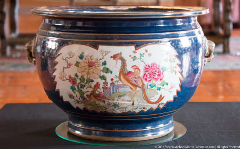 Round cobalt-blue porcelain jardinière with side handles and a white cartouche painted with long-tailed birds, peonies, and foliage.