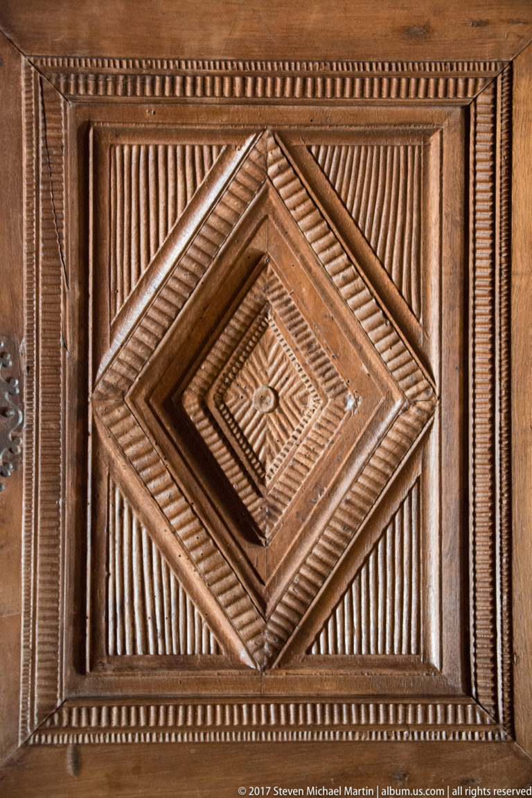 Square carved wooden panel with concentric diamond frames, parallel fluting, beaded borders, and a small central rosette.