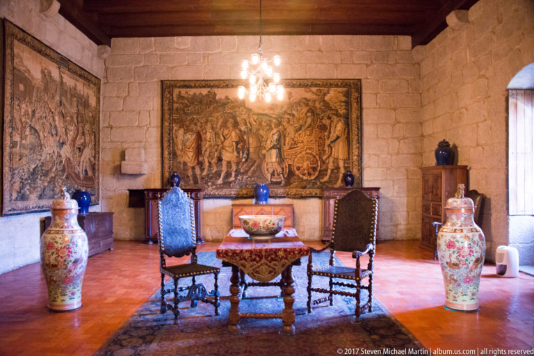 Granite chamber with two high-backed chairs, small table, large tapestries, chandelier, and tall polychrome porcelain jars.